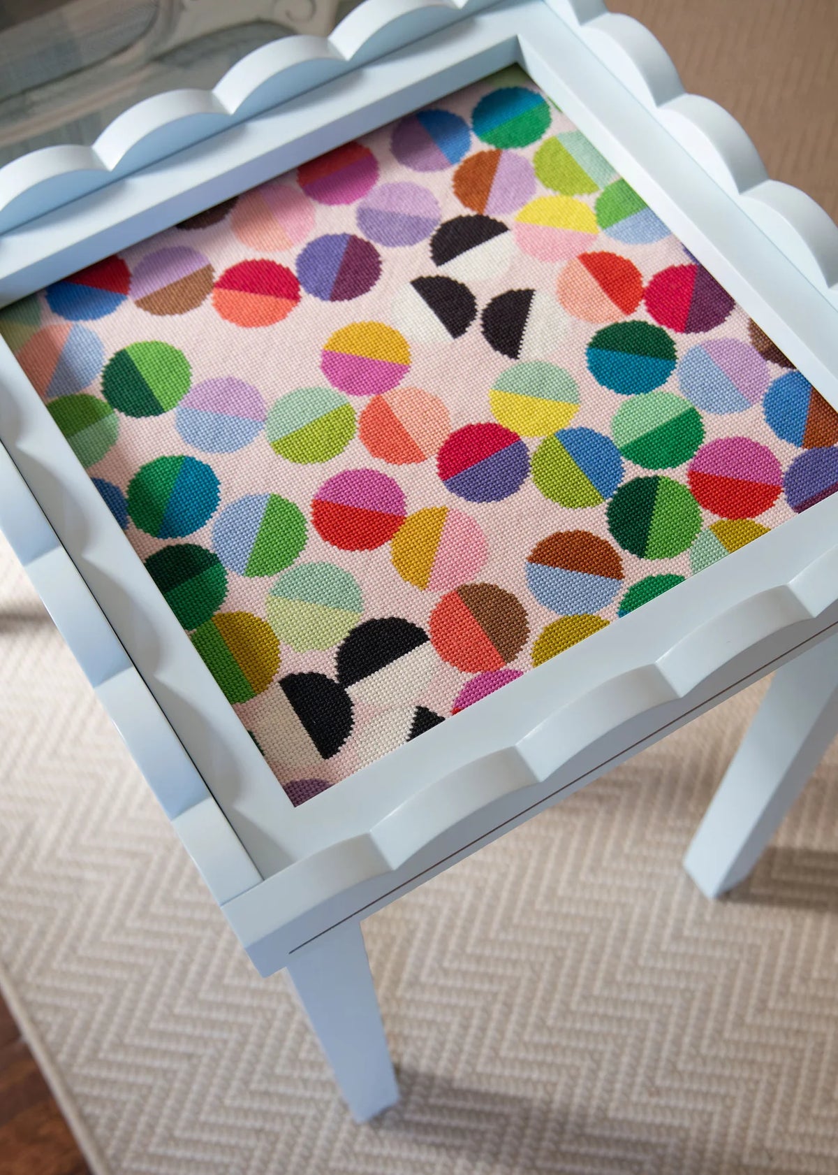 Small table with a colorful polka dot needlepoint canvas top on a neutral background